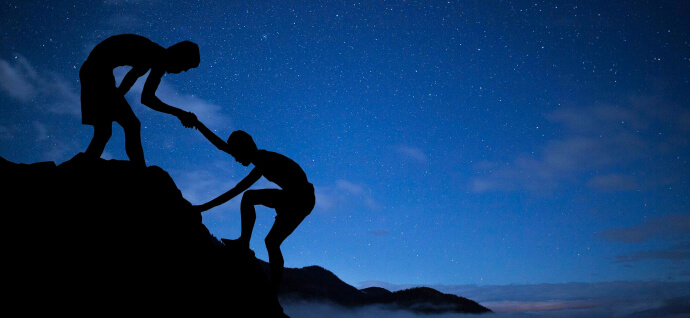 One person helps another climb a mountain